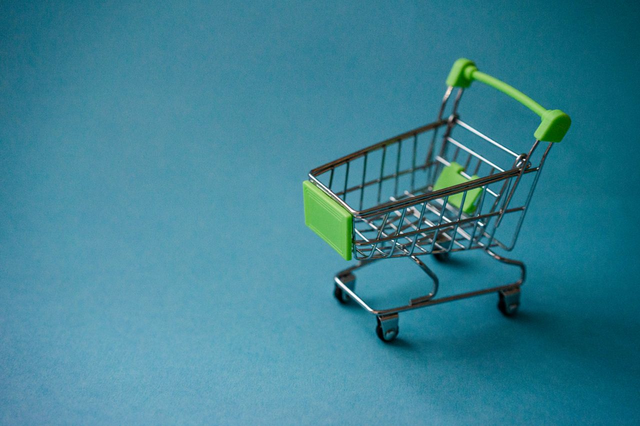 A miniature shopping cart with green accents on a blue background, perfect for retail concepts.